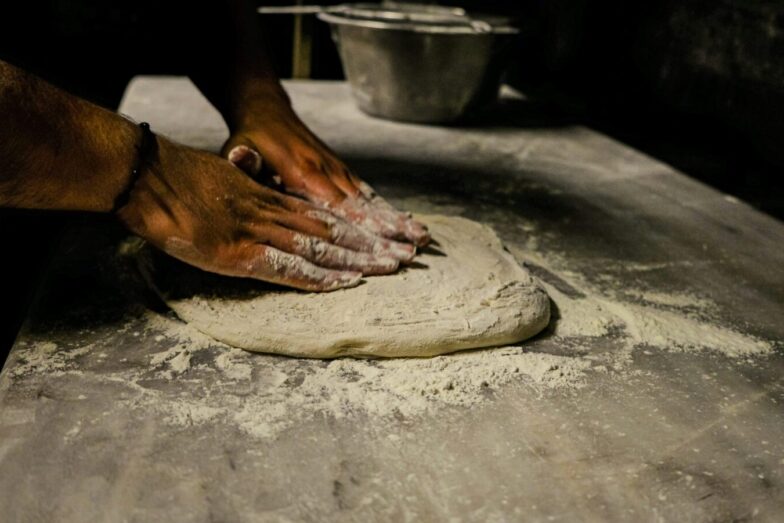 Close-up of a man kneading dough on a floured table in a traditional setting.