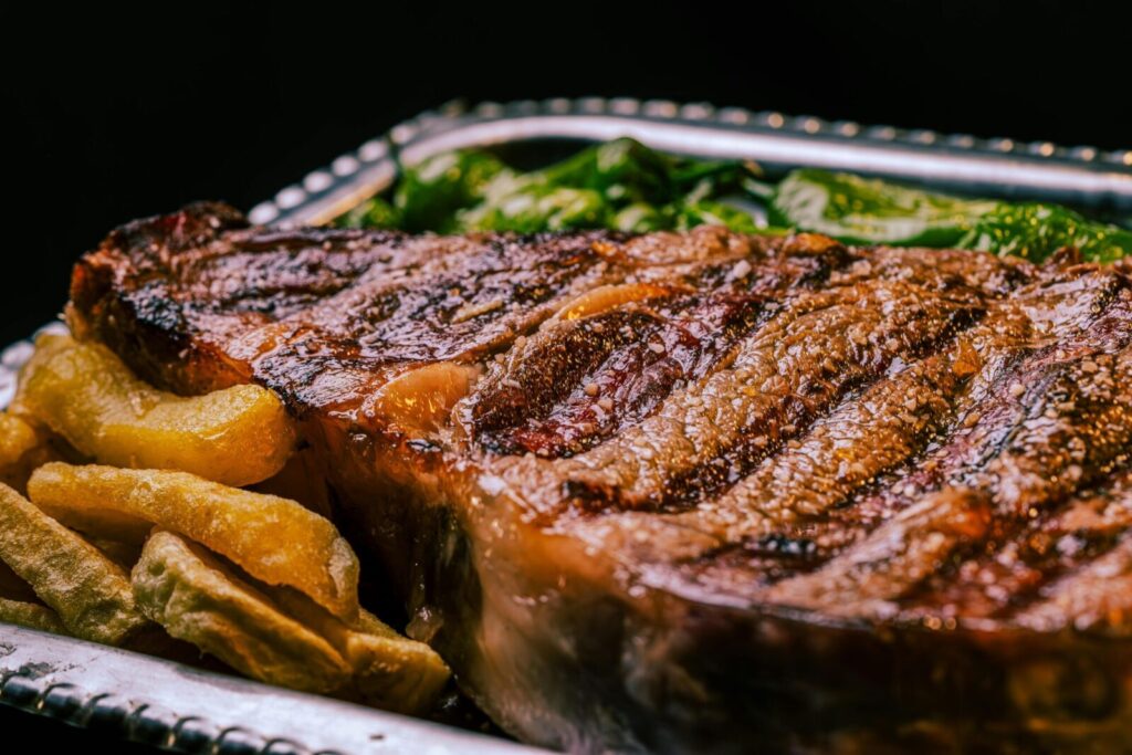 Close-up of a juicy grilled steak with fries and greens. Perfect meal for steak lovers.