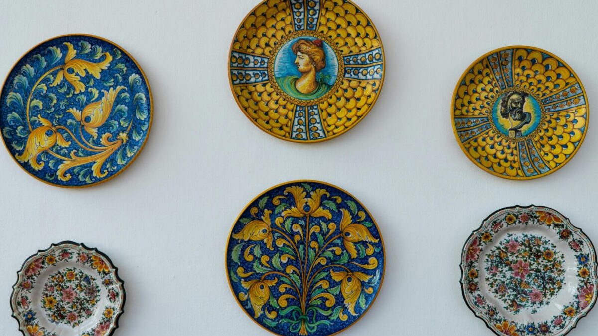 A collection of ornate Italian ceramic plates with vibrant designs and colors displayed on a white wall.