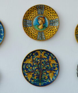 A collection of ornate Italian ceramic plates with vibrant designs and colors displayed on a white wall.