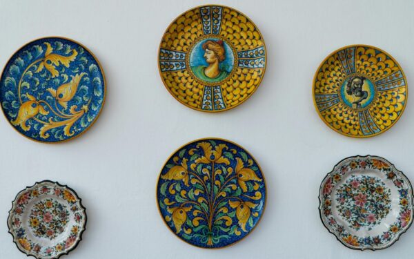 A collection of ornate Italian ceramic plates with vibrant designs and colors displayed on a white wall.