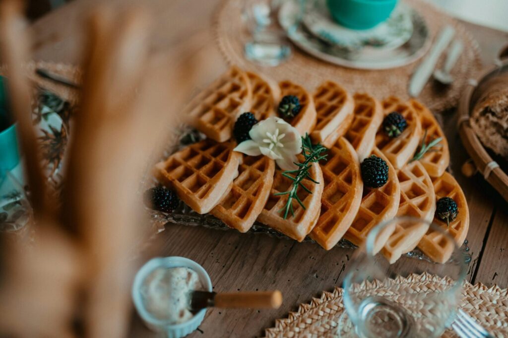 A delightful setup of waffles garnished with blackberries, cream, and a flower on a rustic table.