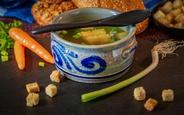 A comforting bowl of vegetable broth with fresh carrots, leeks, and croutons, perfect for a cozy meal.