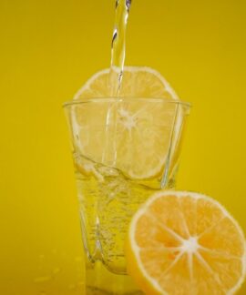A close-up of water pouring into a glass with lemon slices, vibrant yellow backdrop.