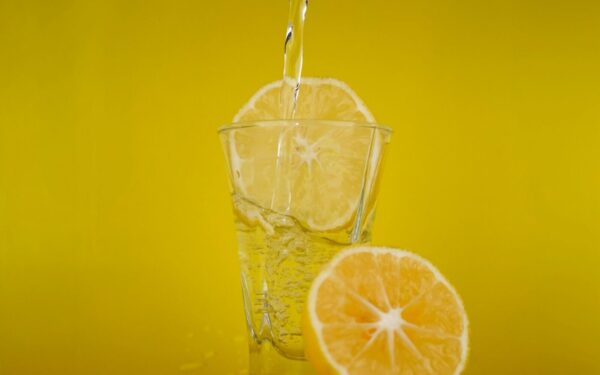 A close-up of water pouring into a glass with lemon slices, vibrant yellow backdrop.