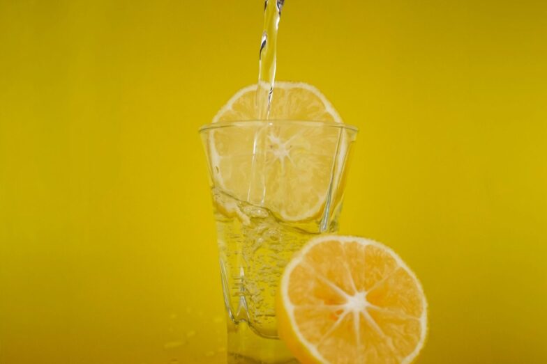 A close-up of water pouring into a glass with lemon slices, vibrant yellow backdrop.
