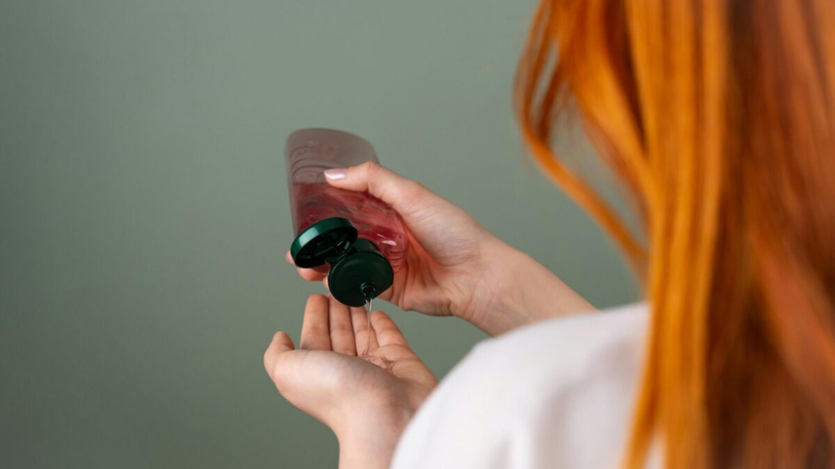 Woman pressing shampoo from a bottle into her hand, highlighting hair care routine.