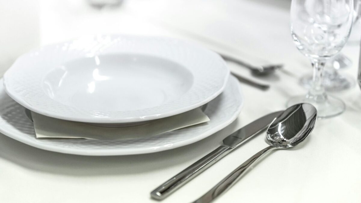 Elegant dining table with white porcelain plates and silver cutlery elegantly arranged.