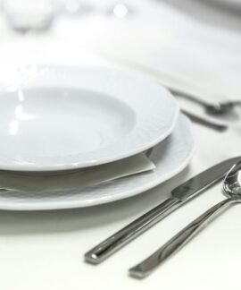 Elegant dining table with white porcelain plates and silver cutlery elegantly arranged.