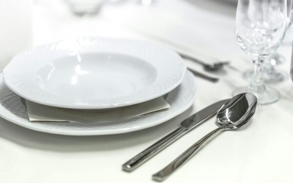 Elegant dining table with white porcelain plates and silver cutlery elegantly arranged.