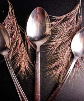 Three metallic spoons creatively arranged with pine leaves on a textured surface.