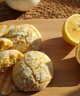 Freshly baked lemon cookies with halved lemons on a wooden platter in sunlight.