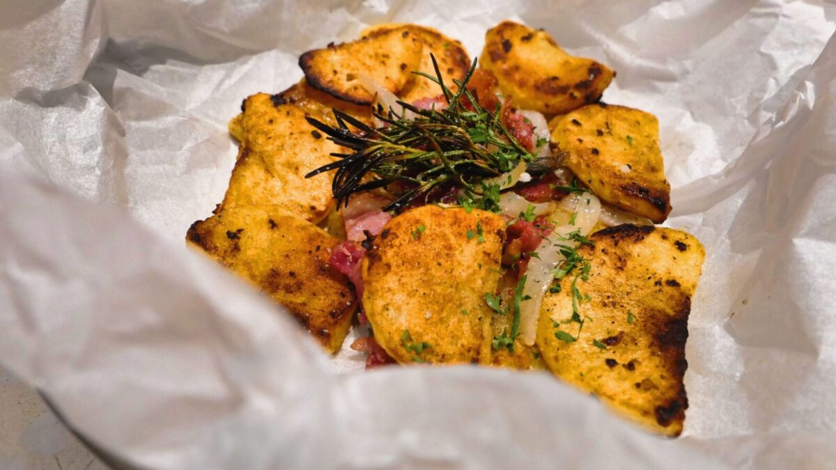 Delicious rustic-style baked potato slices with fresh herbs on parchment paper.
