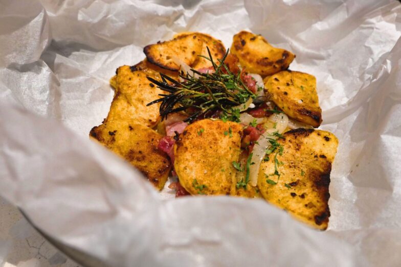 Delicious rustic-style baked potato slices with fresh herbs on parchment paper.