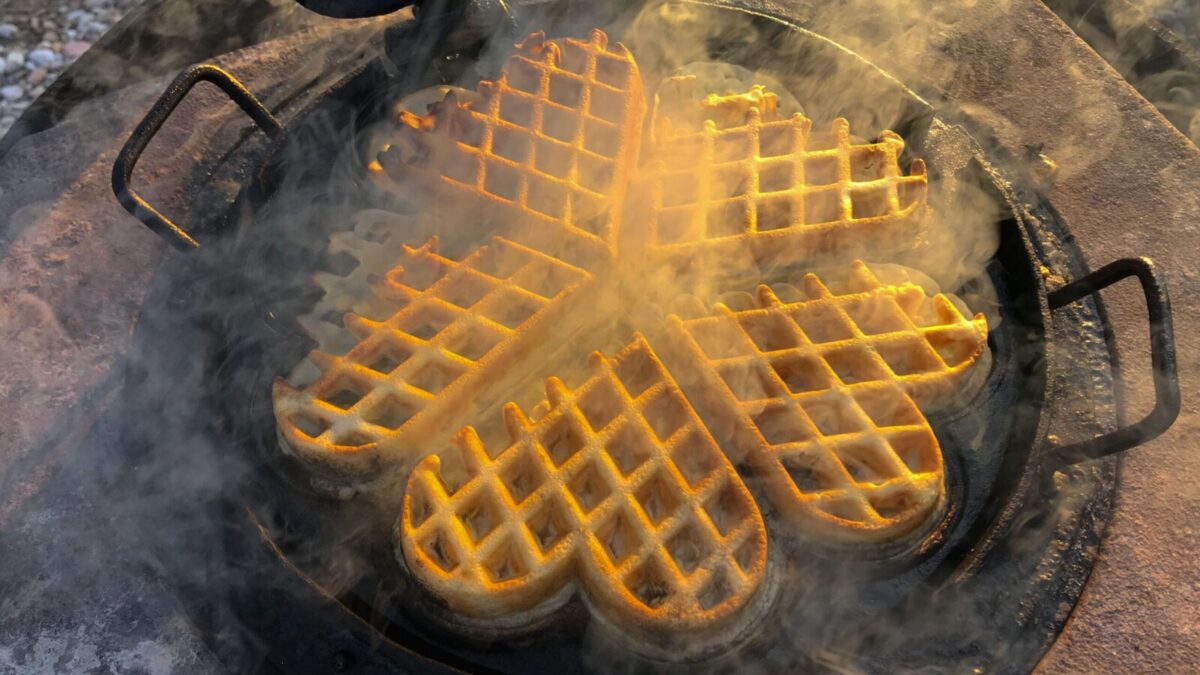 Delicious golden waffles cooking in a heart-shaped cast iron pan with steam.