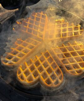 Delicious golden waffles cooking in a heart-shaped cast iron pan with steam.