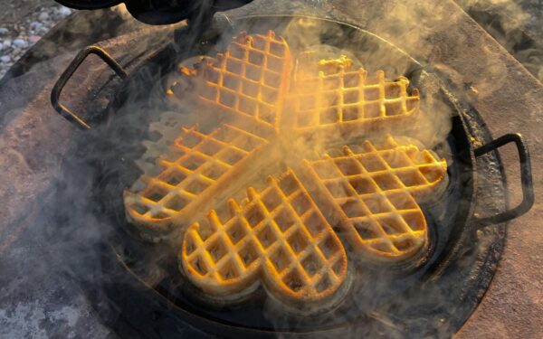 Delicious golden waffles cooking in a heart-shaped cast iron pan with steam.