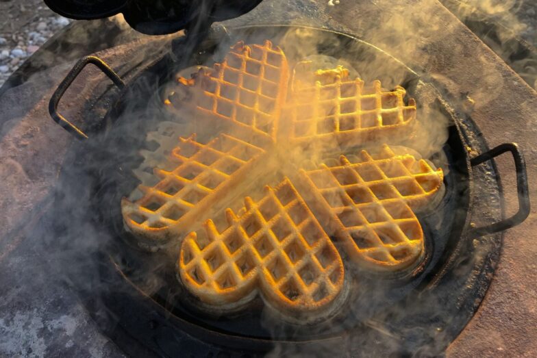 Delicious golden waffles cooking in a heart-shaped cast iron pan with steam.