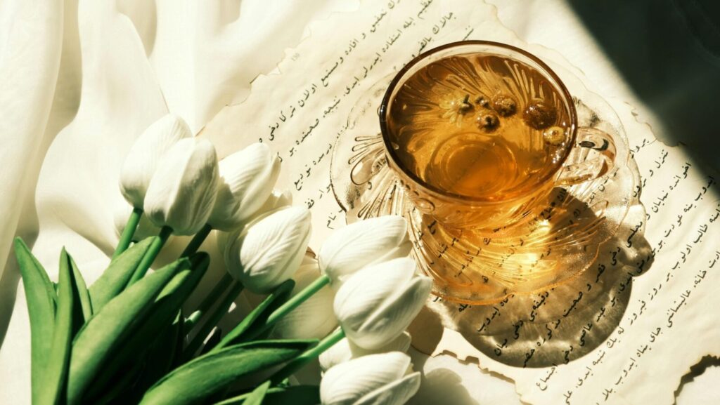 Glass cup of herbal tea and white tulips on paper with calligraphy script, creating a serene aesthetic.
