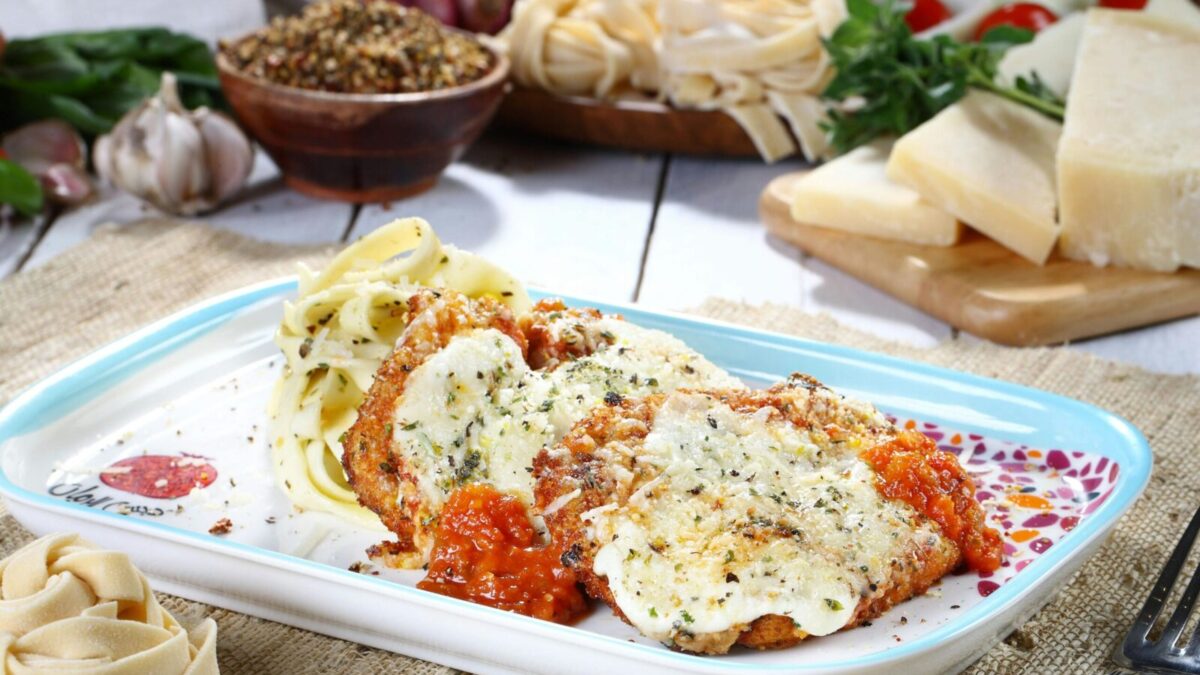 Tasty chicken parmesan with pasta and fresh ingredients on a rustic table.