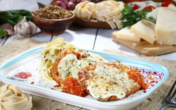 Tasty chicken parmesan with pasta and fresh ingredients on a rustic table.
