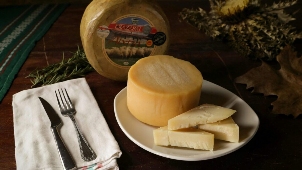 A rustic setting featuring a round Idiazabal cheese with sliced pieces on a plate.