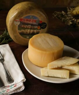 A rustic setting featuring a round Idiazabal cheese with sliced pieces on a plate.