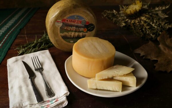 A rustic setting featuring a round Idiazabal cheese with sliced pieces on a plate.