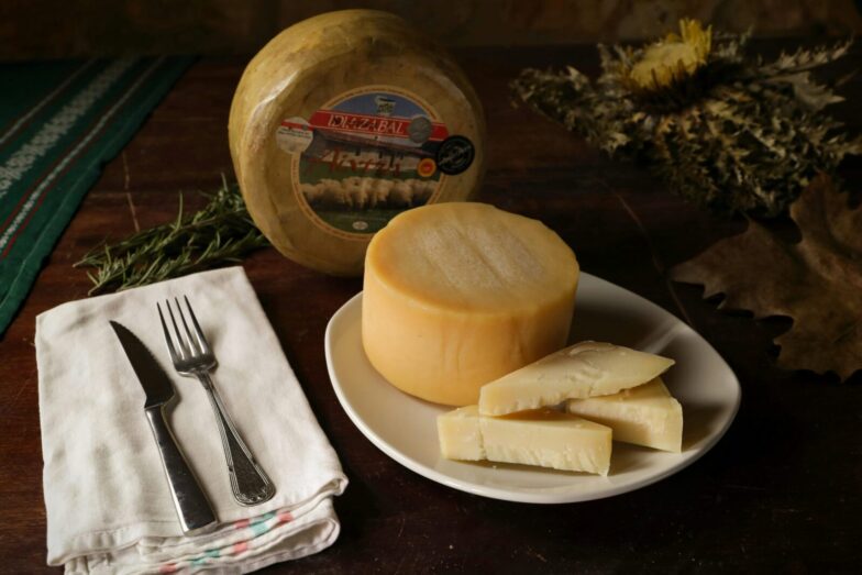 A rustic setting featuring a round Idiazabal cheese with sliced pieces on a plate.