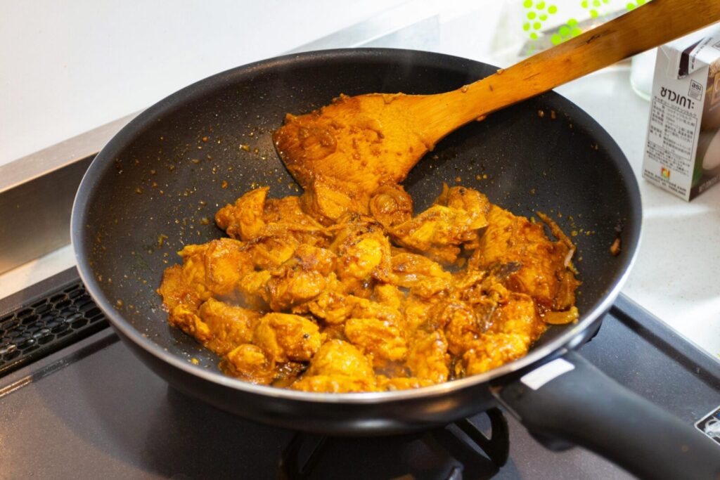 A frying pan filled with spicy curry chicken cooking on a stove, showcasing a rich golden hue.