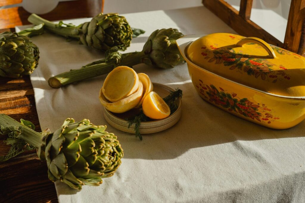 Rustic kitchen scene featuring artichokes, lemons, and a vintage yellow dish in warm sunlight.