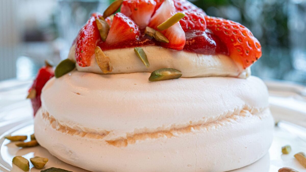 A close-up of a scrumptious strawberry pavlova topped with fresh strawberries and pistachios.