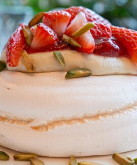 A close-up of a scrumptious strawberry pavlova topped with fresh strawberries and pistachios.
