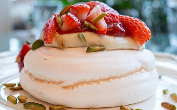 A close-up of a scrumptious strawberry pavlova topped with fresh strawberries and pistachios.