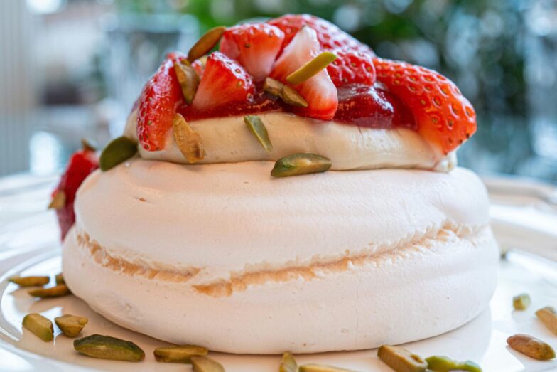 A close-up of a scrumptious strawberry pavlova topped with fresh strawberries and pistachios.
