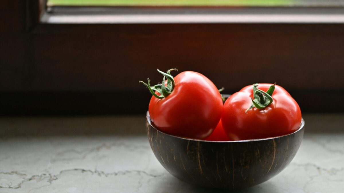 Vibrant red tomatoes in a rustic wooden bowl placed by a sunny window, perfect for illustrating organic freshness.