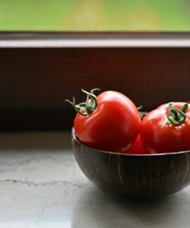 Vibrant red tomatoes in a rustic wooden bowl placed by a sunny window, perfect for illustrating organic freshness.