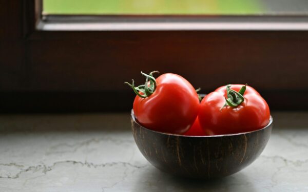 Vibrant red tomatoes in a rustic wooden bowl placed by a sunny window, perfect for illustrating organic freshness.