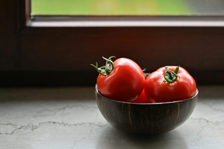 Vibrant red tomatoes in a rustic wooden bowl placed by a sunny window, perfect for illustrating organic freshness.