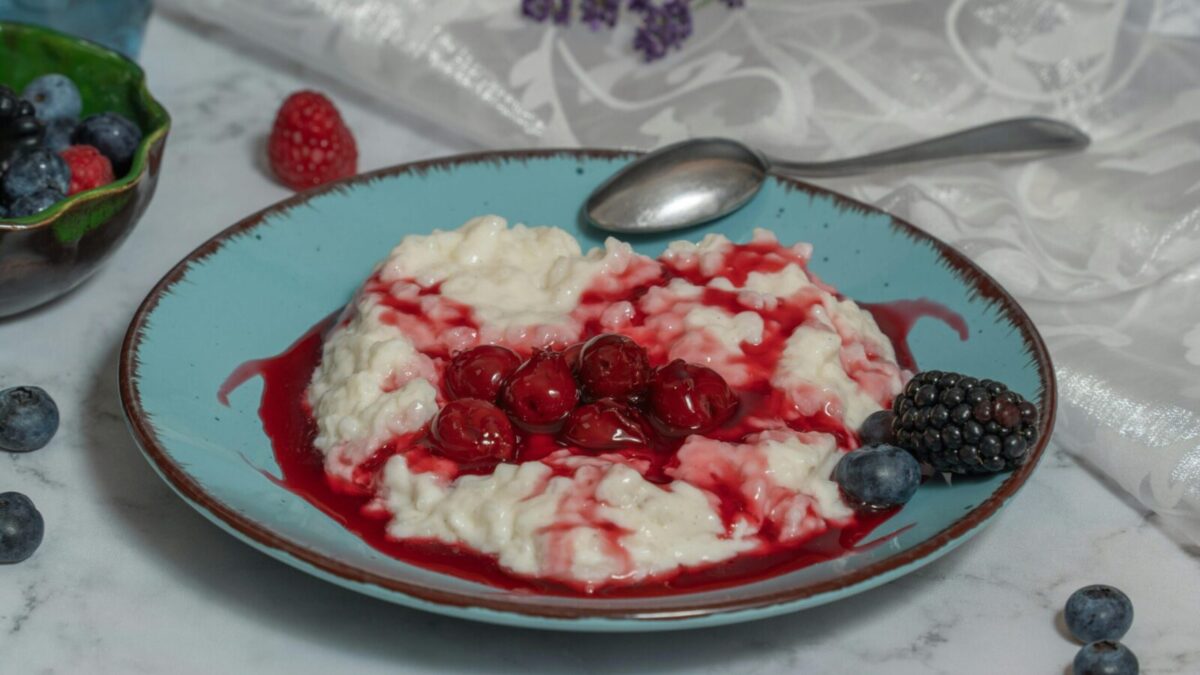 A delectable rice porridge with fresh berries and cherry sauce on a ceramic plate.