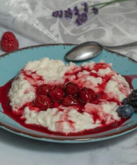 A delectable rice porridge with fresh berries and cherry sauce on a ceramic plate.
