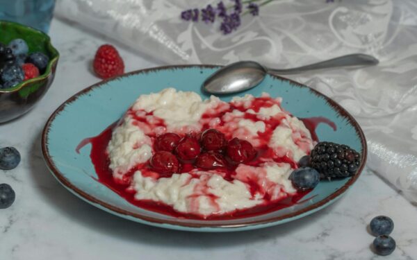 A delectable rice porridge with fresh berries and cherry sauce on a ceramic plate.