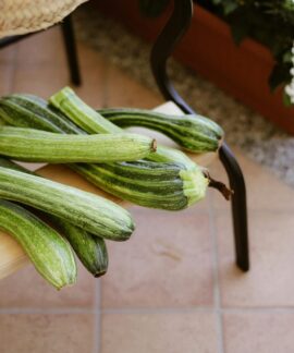 A collection of fresh green zucchinis displayed on a wooden bench outdoors.