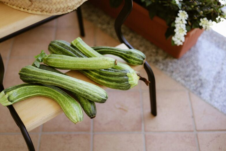 A collection of fresh green zucchinis displayed on a wooden bench outdoors.
