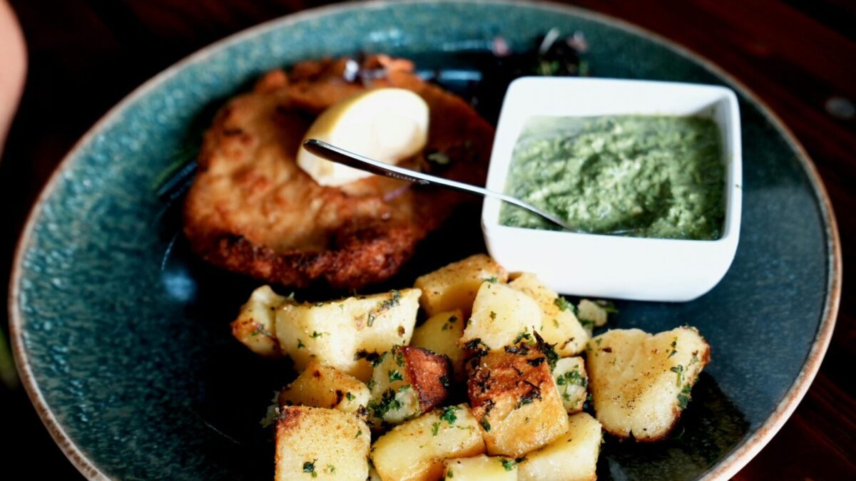 Plate of schnitzel, roasted potatoes, and green sauce, garnished with a lemon wedge.