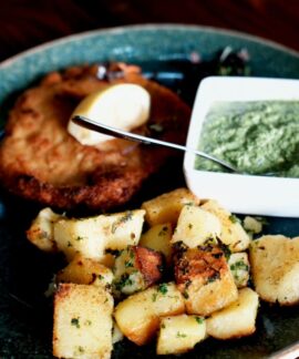Plate of schnitzel, roasted potatoes, and green sauce, garnished with a lemon wedge.