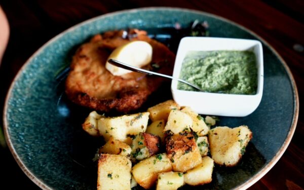 Plate of schnitzel, roasted potatoes, and green sauce, garnished with a lemon wedge.