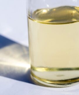 A close-up image of a glass bottle with liquid, showcasing light reflection and shadow on a white surface.