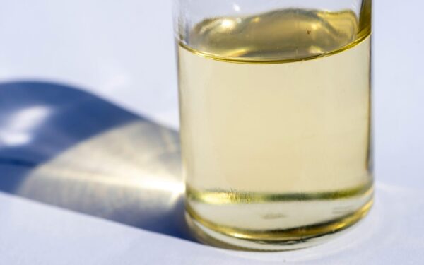 A close-up image of a glass bottle with liquid, showcasing light reflection and shadow on a white surface.