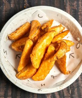 Golden crispy potato wedges served in a rustic white bowl on wood.